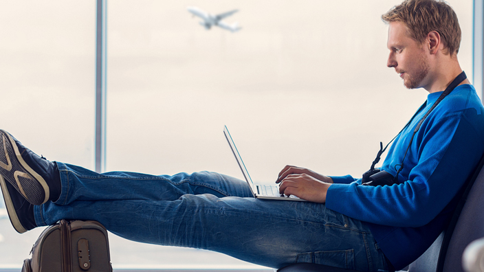 A man types on a laptop computer while waiting in an airport