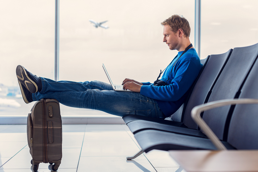 A man types on a laptop computer while waiting in an airport