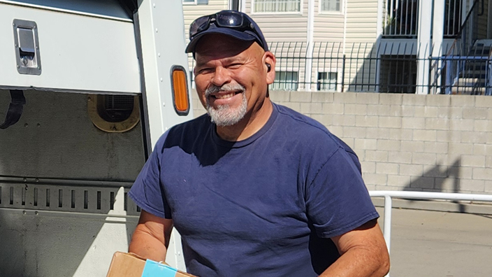 A USPS employee unloads packages from the back of USPS delivery vehicle.