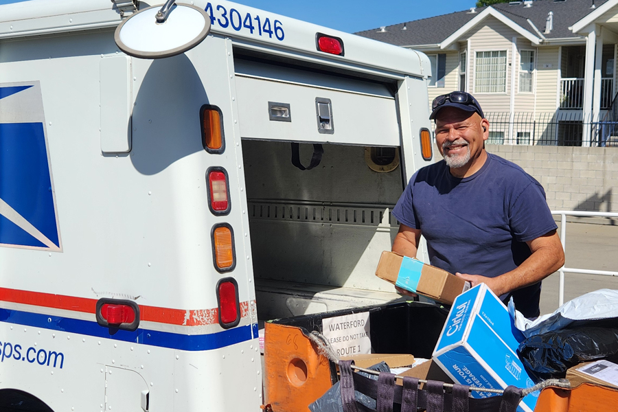 A USPS employee unloads packages from the back of USPS delivery vehicle.