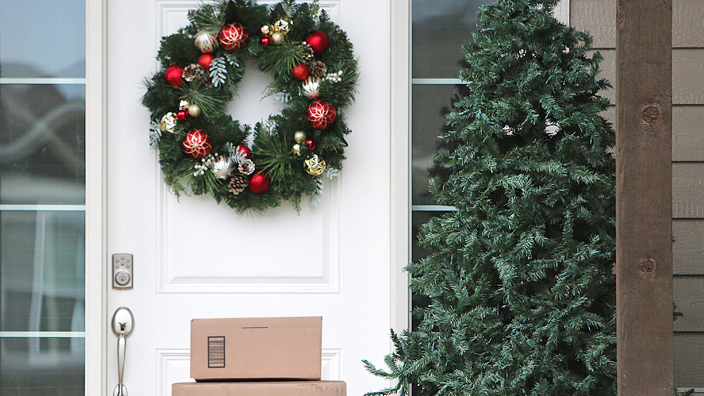 A stack of packages in front of a door to a home decorated for the holidays