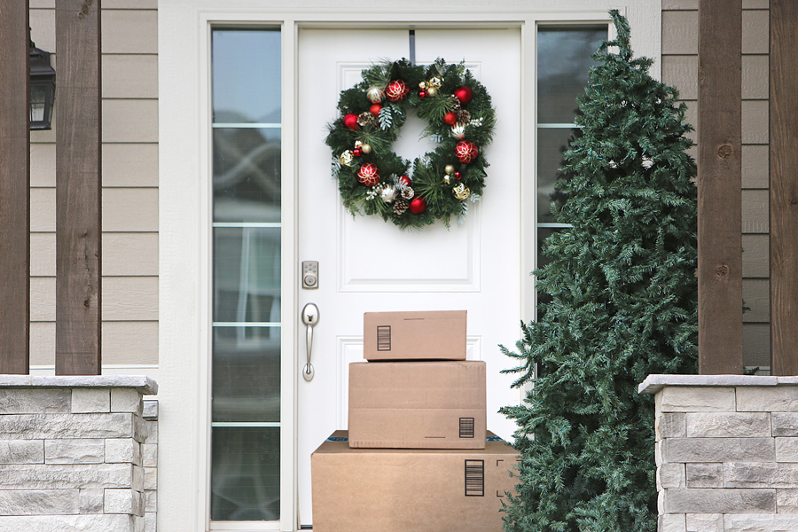 A stack of packages in front of a door to a home decorated for the holidays