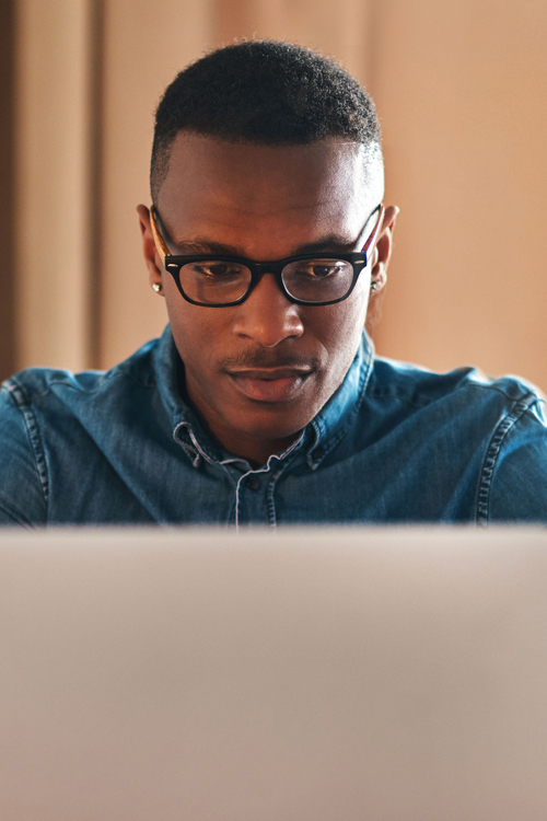 A man wearing glasses works on a laptop computer.