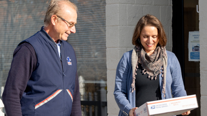 A customer receives a package from a USPS letter carrier.