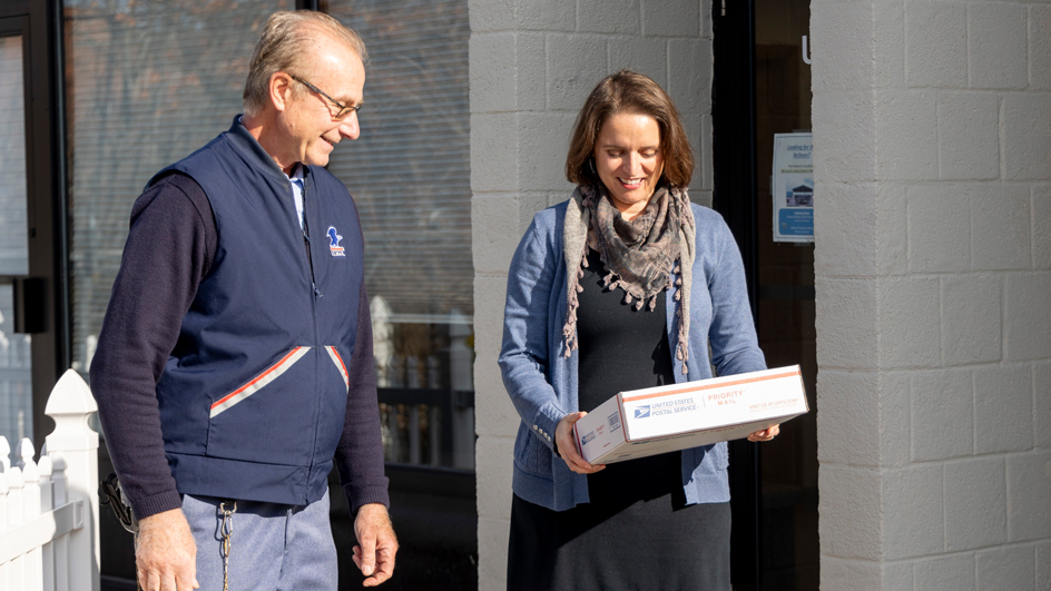 A customer receives a package from a USPS letter carrier.