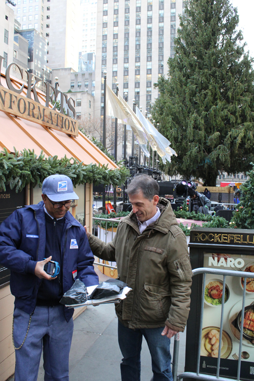 A USPS letter carrier scans a package with a handheld device before handing it to a customer.