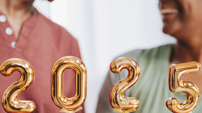 smiling middle-aged couple hold small gold balloons that spell out the year 2025