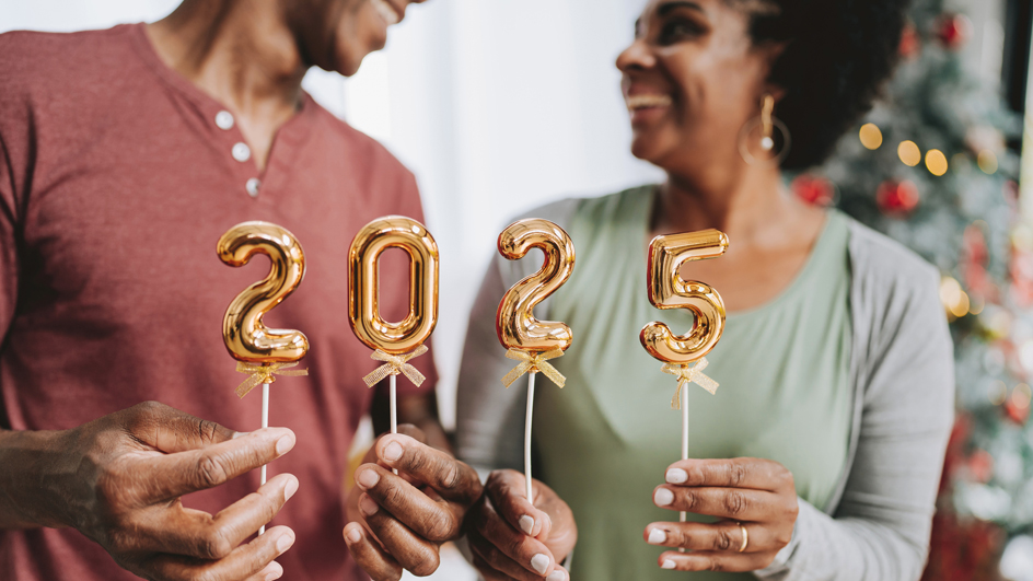 smiling middle-aged couple hold small gold balloons that spell out the year 2025