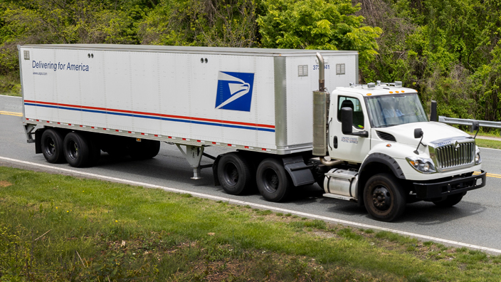 A USPS semi truck driving on a road.