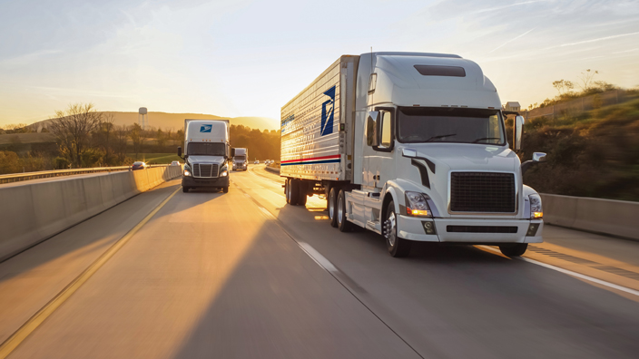 Three USPS-branded tractor-trailers move along a highway