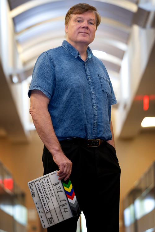 A man dressed in a denim shirt and black pants holds a clapboard from a movie set that bears the film title “Brass Band”