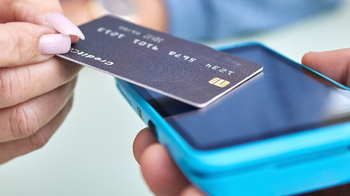 A woman taps a credit card on a handheld scanner.