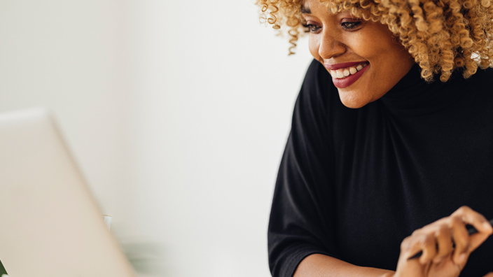 A woman wearing a black blouse smiles while looking at a laptop computer