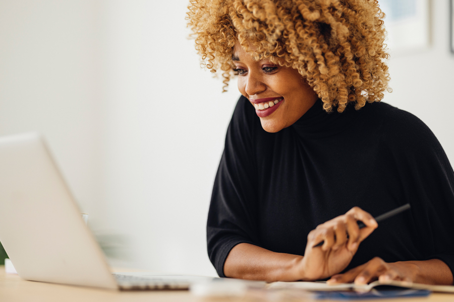 A woman wearing a black blouse smiles while looking at a laptop computer