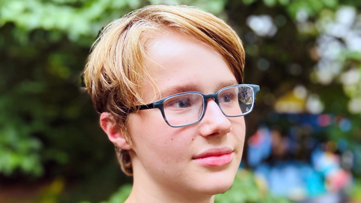 A smiling boy wearing eyeglasses looks off camera