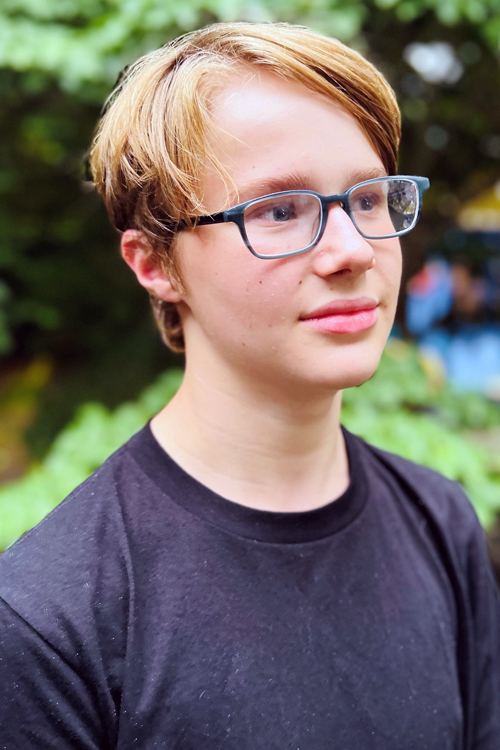 A smiling boy wearing eyeglasses looks off camera