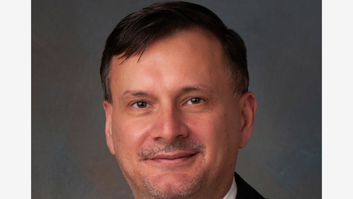 A studio portrait of a smiling man wearing a business suit and tie