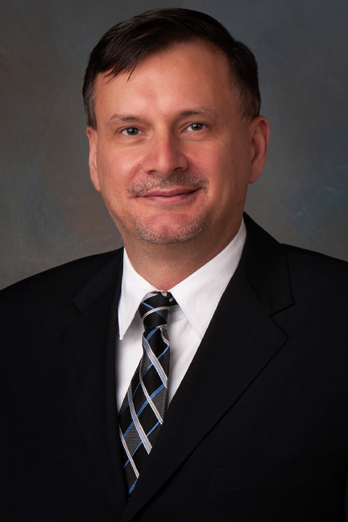 A studio portrait of a smiling man wearing a business suit and tie