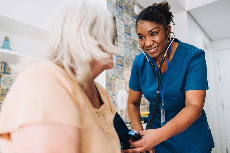 A nurse takes the blood pressure of an elderly woman in the bedroom of an assisted living setting.