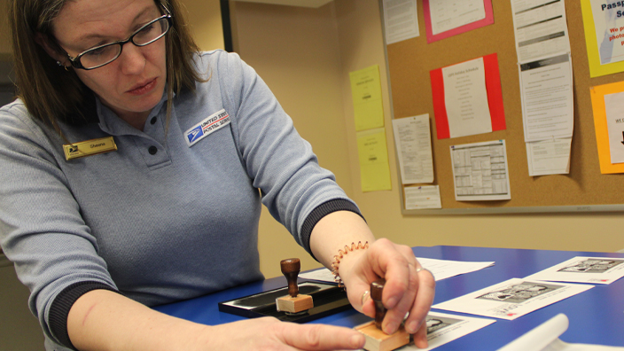 A woman in a USPS retail uniform hand cancels an envelope