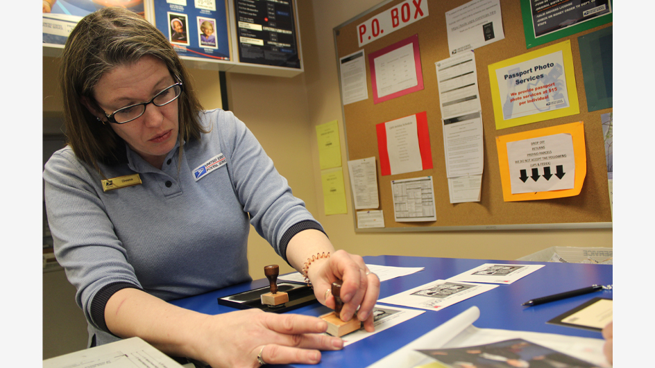 A woman in a USPS retail uniform hand cancels an envelope