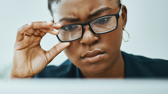 A woman with a skeptical facial expression looks at a computer monitor screen.