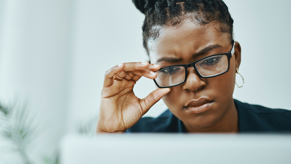 A woman with a skeptical facial expression looks at a computer monitor screen.