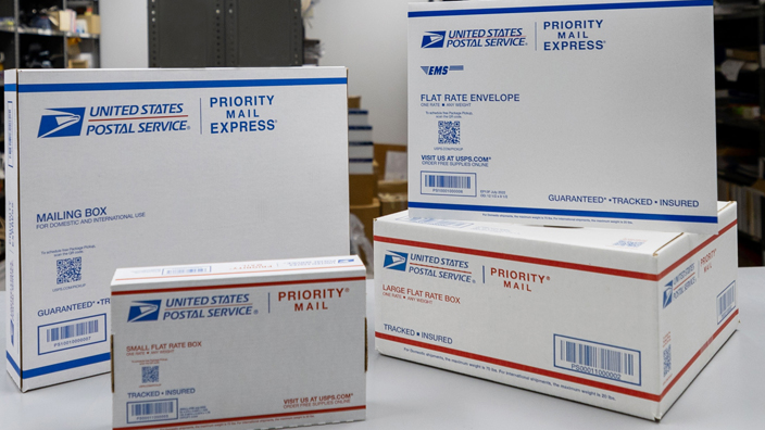 A stack of USPS-branded boxes stacked on a table in a Post Office workroom