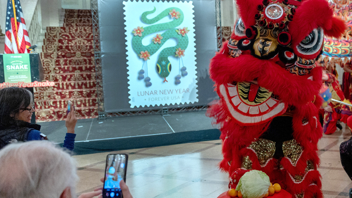 People sitting in an audience use their smartphones to record a large costumed dragon performing on a stage