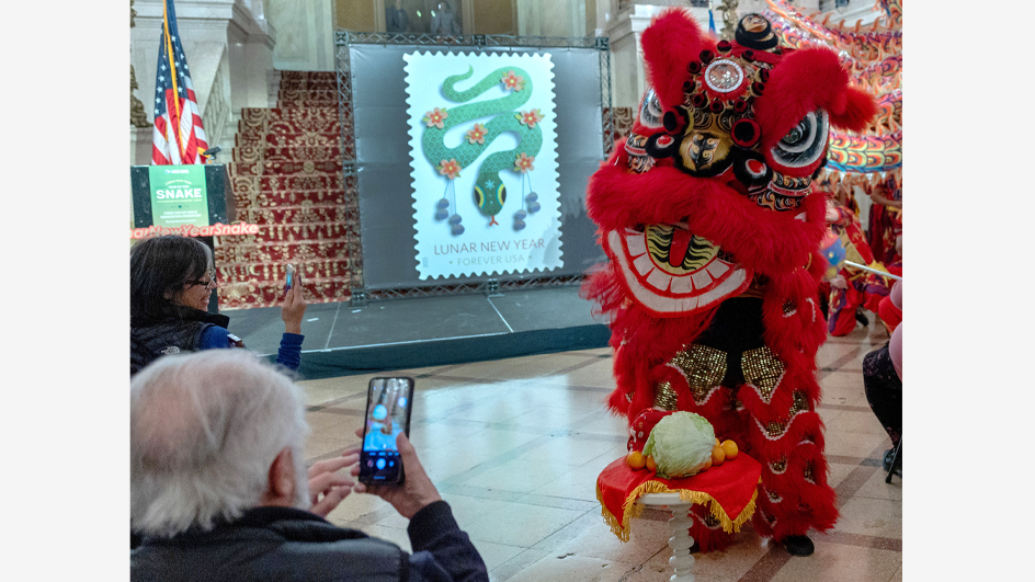 People sitting in an audience use their smartphones to record a large costumed dragon performing on a stage