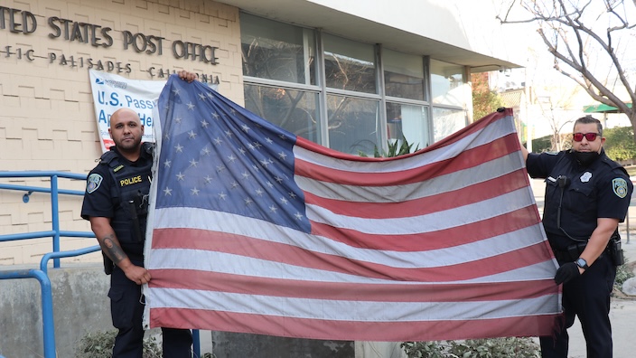 Two police officers hold a U.S. flag aloft in the parking lot of a damaged Post Office building