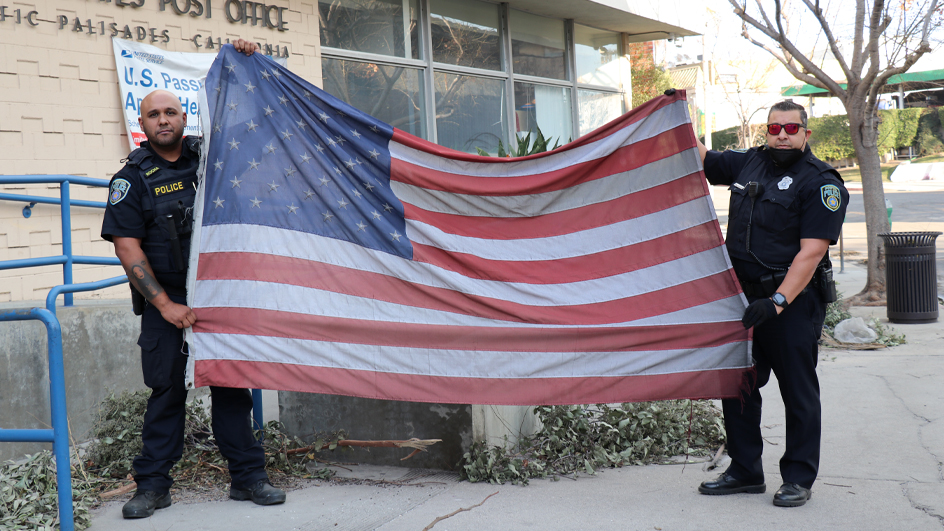 Two police officers hold a U.S. flag aloft in the parking lot of a damaged Post Office building