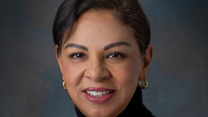 A studio photo of a smiling woman in a maroon jacket