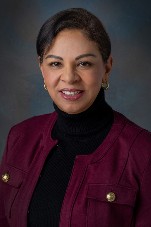 A studio photo of a smiling woman in a maroon jacket