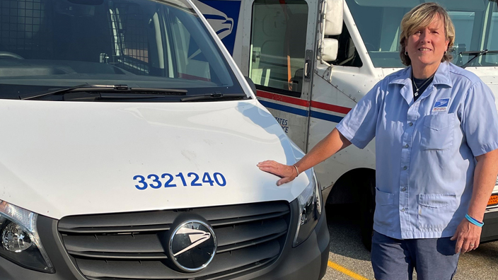 A woman stands next to a USPS delivery truck