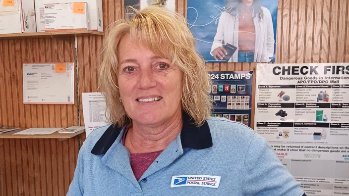 A woman wearing a light blue USPS shirt with dark blue collars and cuffs