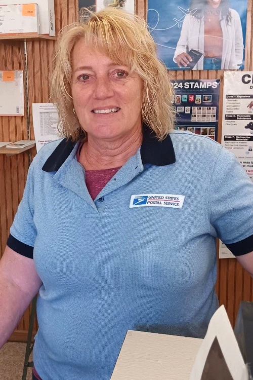 A woman wearing a light blue USPS shirt with dark blue collars and cuffs