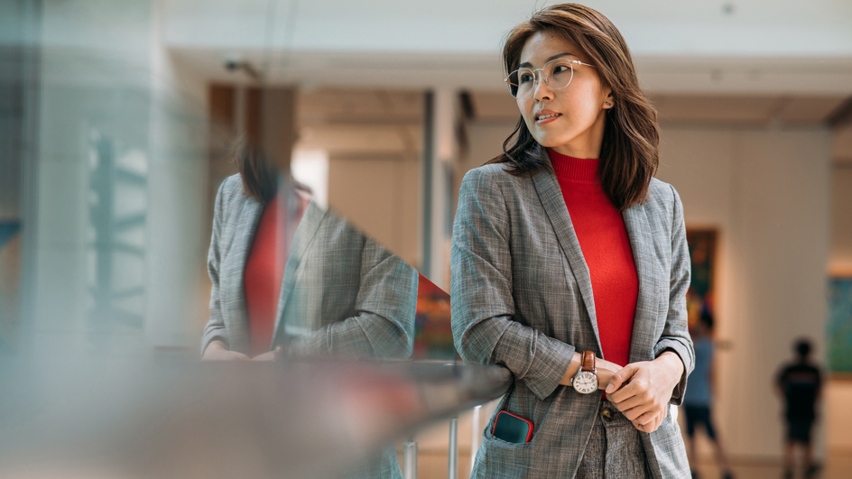 A woman in a gray business suit and red top stands in an office environment