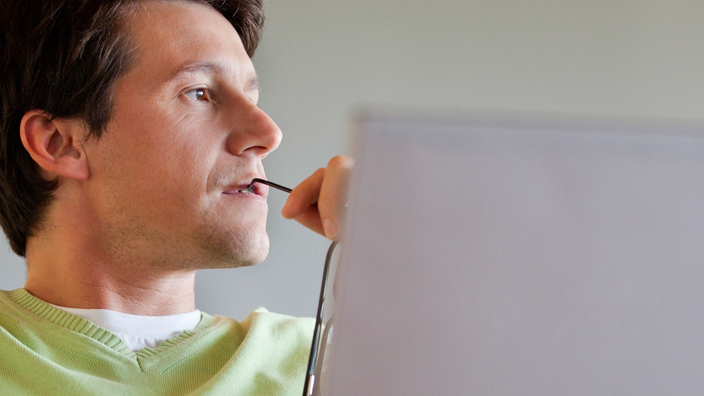 A man with a contemplative expression sits in front of a computer