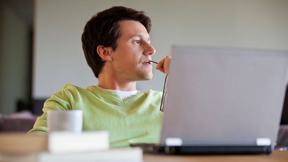 A man with a contemplative expression sits in front of a computer