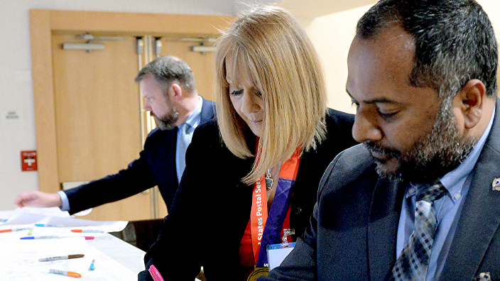 Three people in business suits sign large banners spread on a table