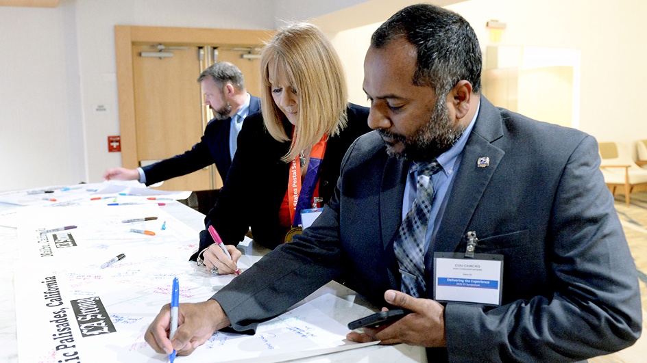 Three people in business suits sign large banners spread on a table