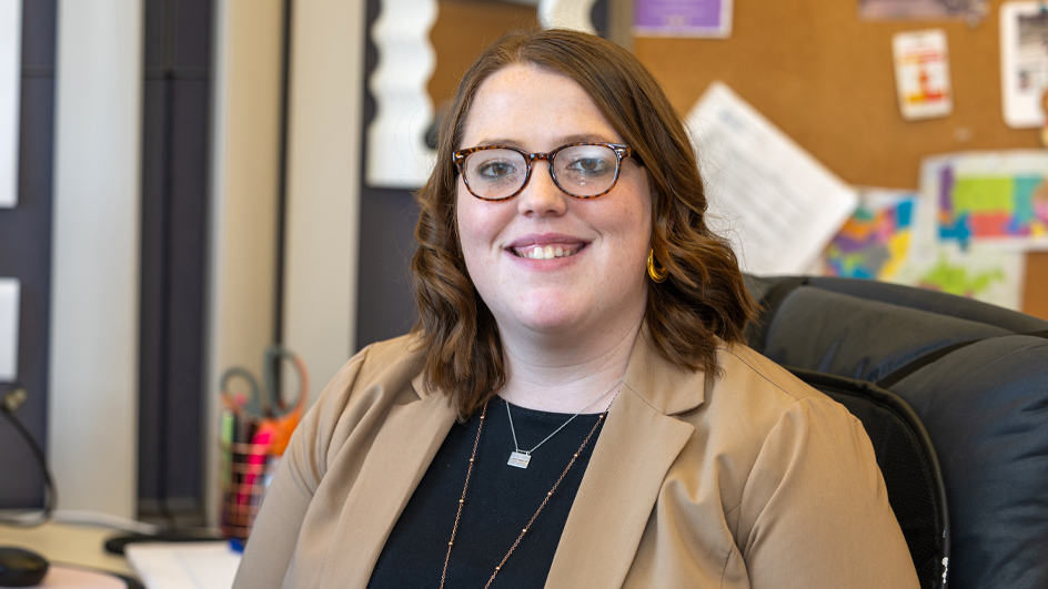 A woman dressed in a suit jacket sits at her desk and smiles brightly