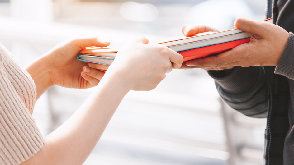 A pair of hands giving a stack of reports to another pair of hands