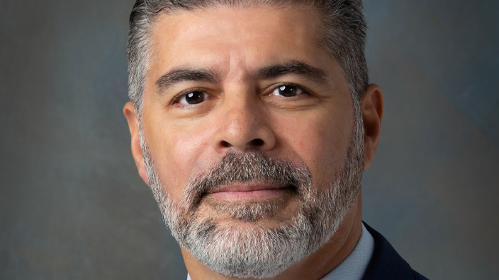 A studio photo of a smiling man in a business suit and tie