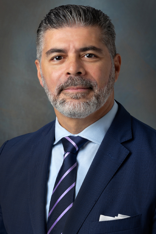 A studio photo of a smiling man in a business suit and tie