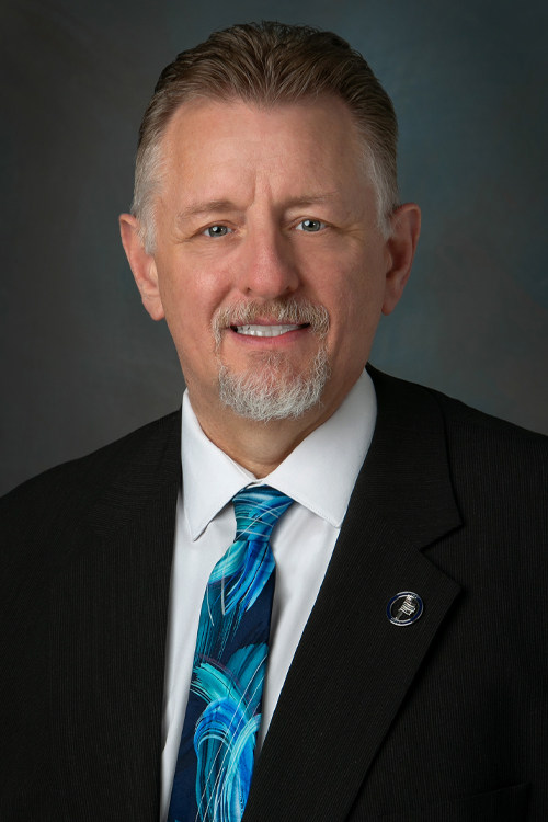 A studio portrait of a smiling man wearing a business suit and tie