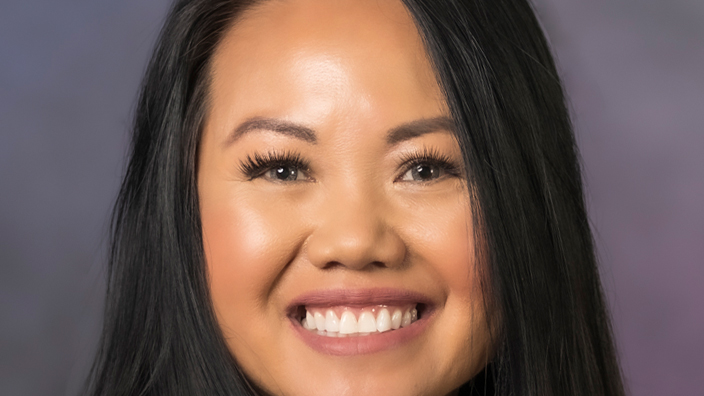 A studio portrait of a smiling woman dressed in a business suit