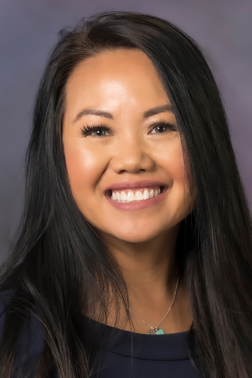 A studio portrait of a smiling woman dressed in a business suit