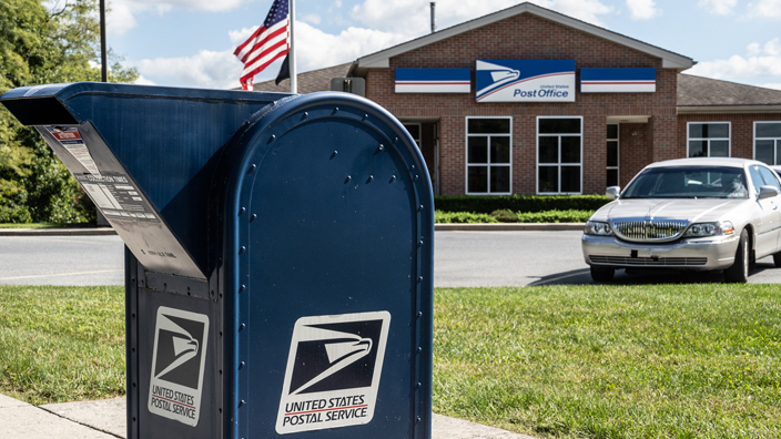 A blue collection box on a sidewalk outside a suburban Post Office